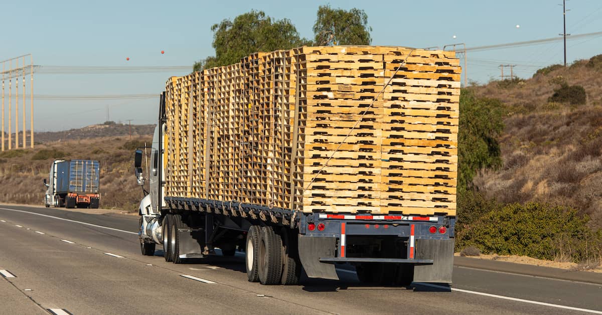a truck drives with a large load of wooden pallets | Coplan and Crane