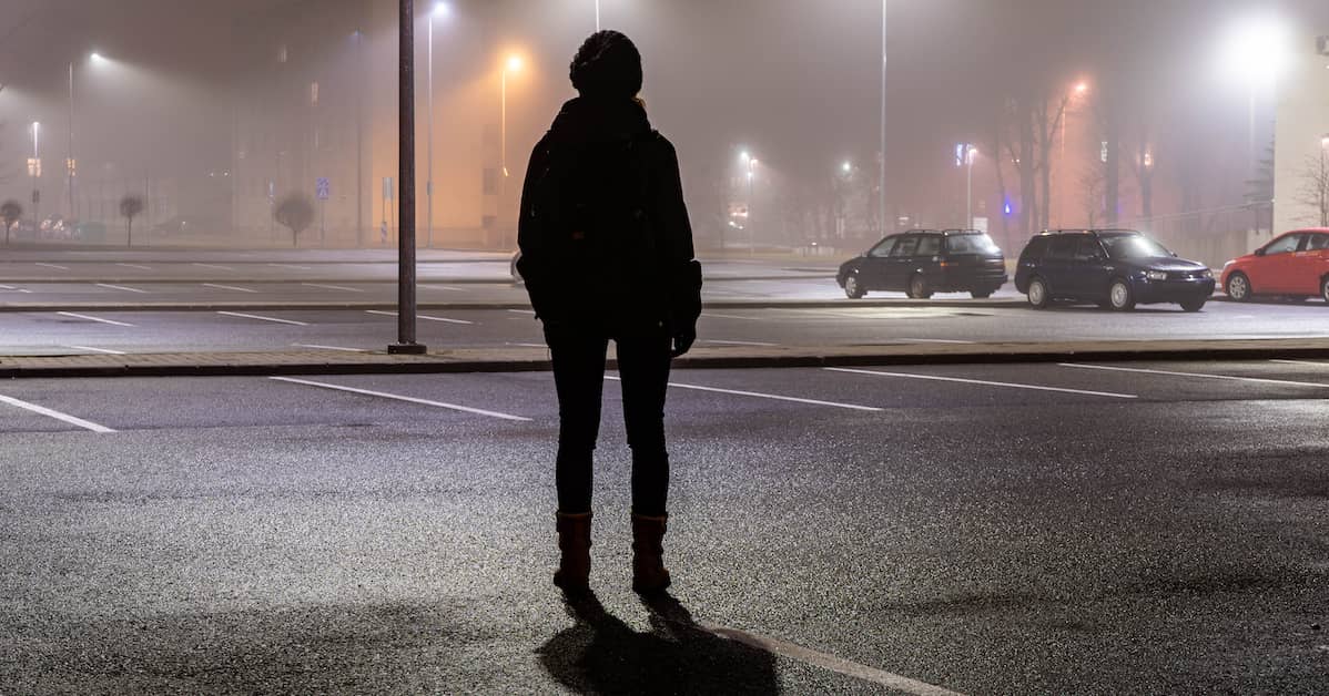 a lone figure stands in a dark parking lot | Coplan and Crane